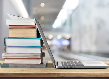 Stack of books beside an open laptop on a desk, representing math tutoring, homework help, and virtual learning.