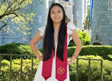 Professional math tutor wearing a graduation sash while standing in a wooded park, representing her educational background and commitment to student success.